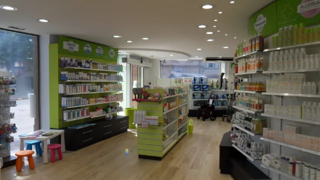 Pharmacie côté vitrine, petite table et tabourets colorés, spots encastrés allumés au plafond
