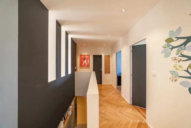 Palier en parquet à bâtons rompus, mur anthracite à ouvertures verticales, spots encastrés allumés