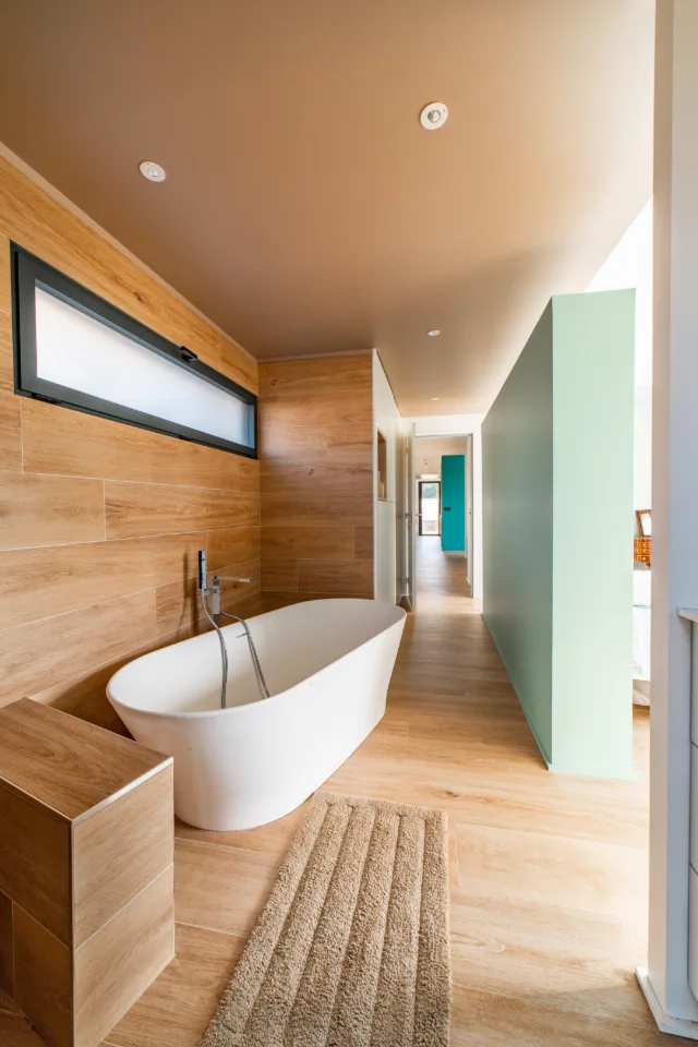 Salle de bain avec baignoire îlot, carrelage effet bois, fenêtre en bandeau et spots encastrés