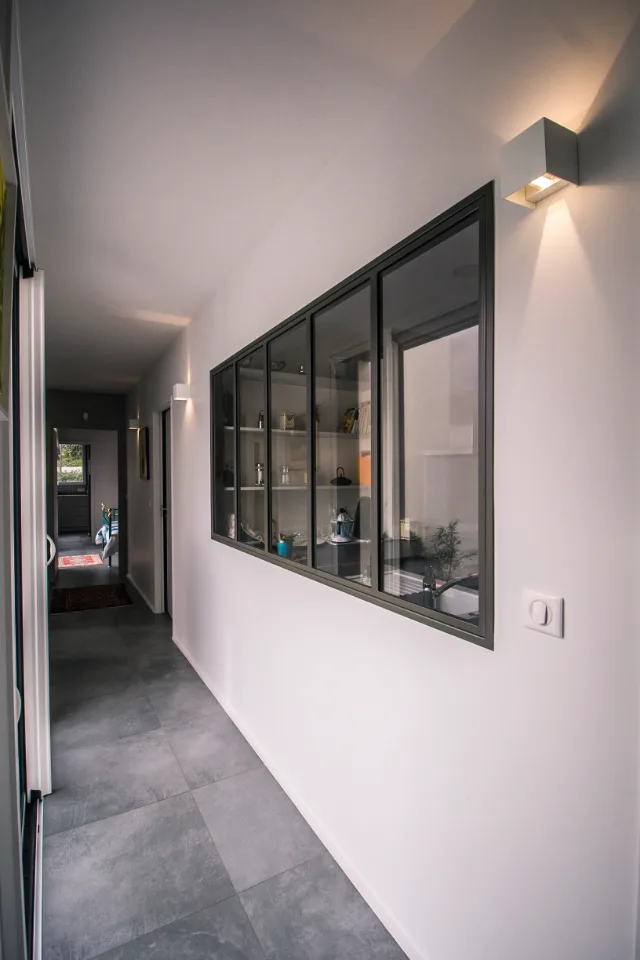 Couloir carrelé avec verrière d’atelier sur la cuisine, appliques cubiques allumées et interrupteur