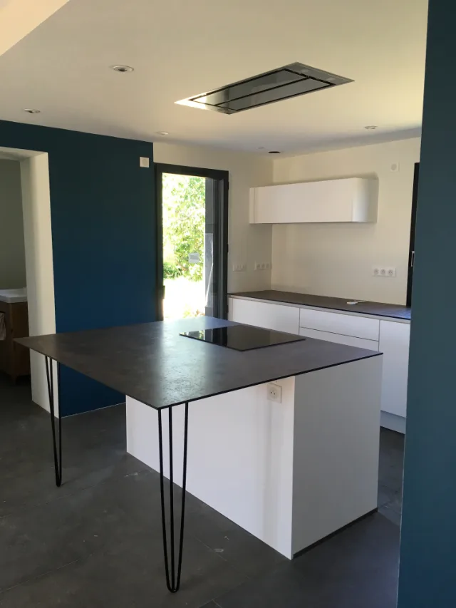 Cuisine aux murs bleus, îlot avec plaque de cuisson sous hotte de plafond, prises sur crédence