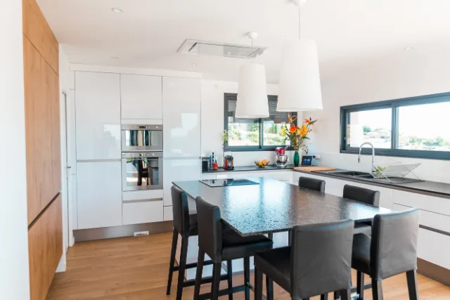 Cuisine blanche laquée, îlot avec plaque de cuisson, deux grandes suspensions et hotte de plafond