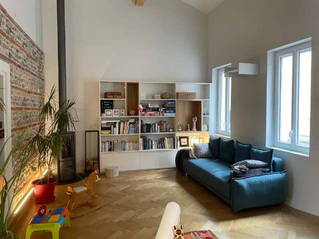 Séjour au mur de briques et galets éclairé en pied, poêle à bois et canapé bleu