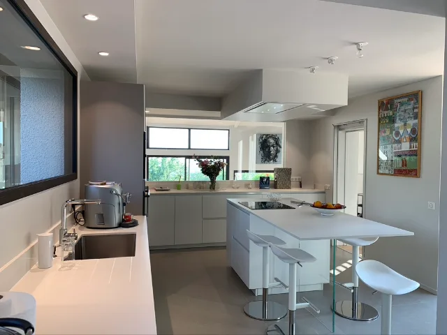 Cuisine blanche, îlot avec plaque de cuisson sous hotte intégrée au plafond, spots encastrés allumés