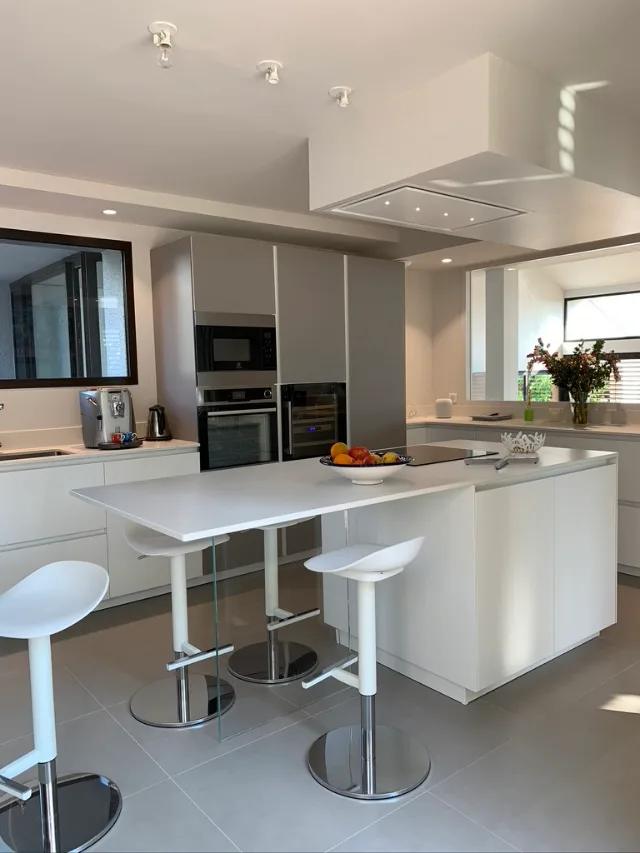 Cuisine blanche avec îlot, colonne four, micro-ondes et cave à vin, hotte intégrée au plafond