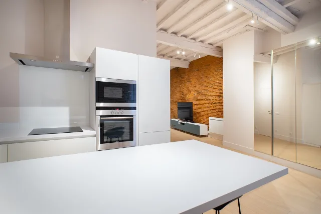 Cuisine blanche avec plaque de cuisson, hotte inox et four encastré, mur de briques au fond