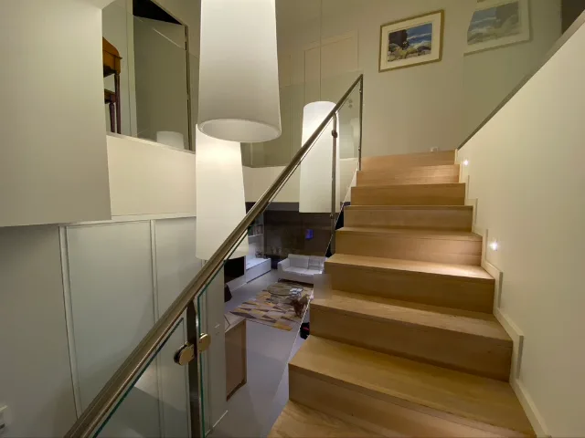 Volée d’escalier en bois, garde-corps vitré, suspensions allumées et balisage lumineux encastré