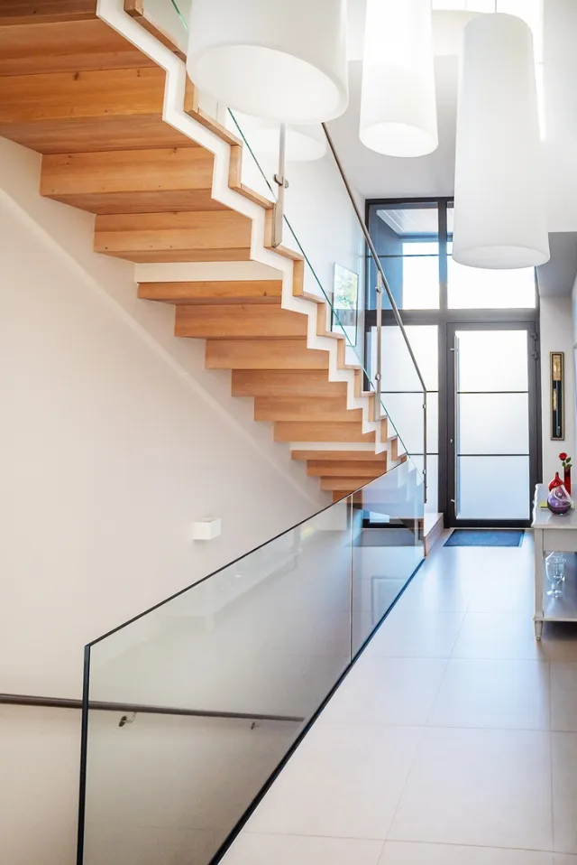Hall avec escalier en bois à garde-corps vitré, grandes suspensions cylindriques et porte vitrée