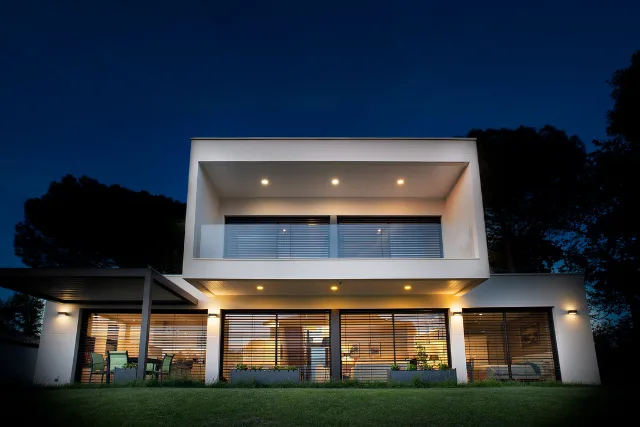 Maison contemporaine blanche à la nuit tombée, spots en sous-face et appliques murales allumés