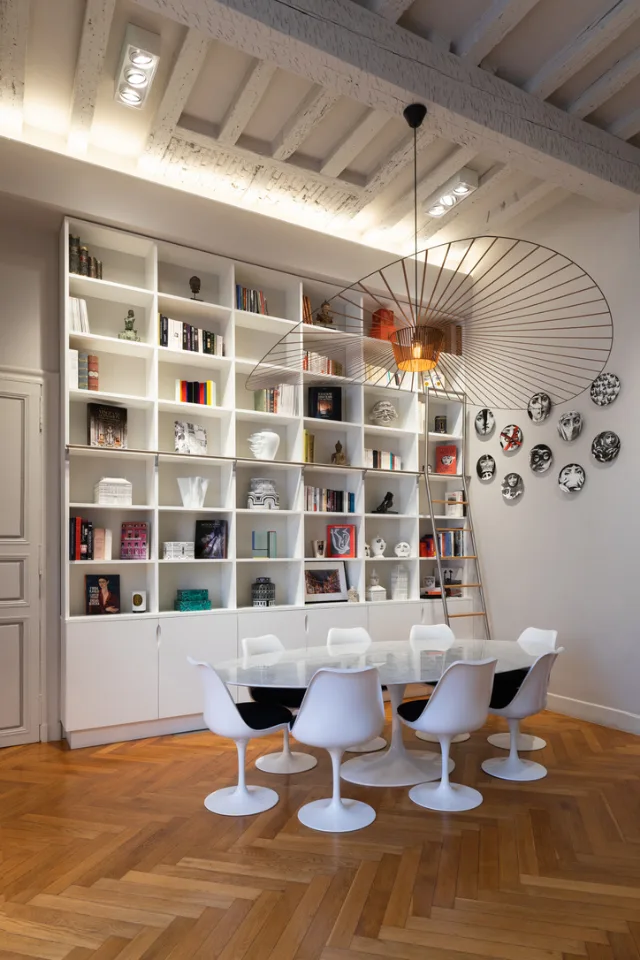 Salle à manger sous poutres, grande suspension filaire, bibliothèque blanche et projecteurs multi-spots allumés
