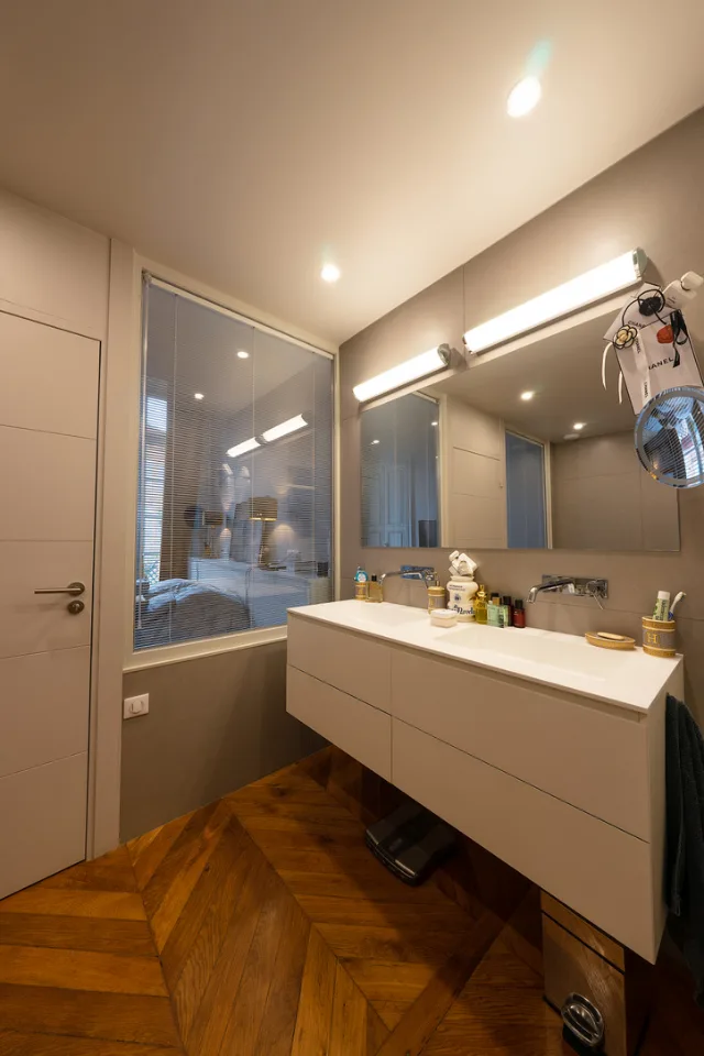 Salle de bains, vasque suspendue, miroir sous deux réglettes allumées, spots encastrés et cloison vitrée