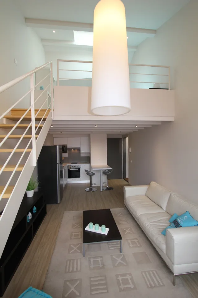 Séjour double hauteur avec mezzanine, grande suspension cylindrique allumée et cuisine sous la mezzanine
