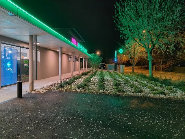 Façade de pharmacie de nuit, auvent bordé de LED vertes, enseigne rose et croix lumineuse
