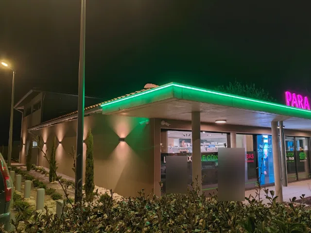 Angle de façade commerciale de nuit, auvent bordé de LED vertes, enseigne rose et appliques murales