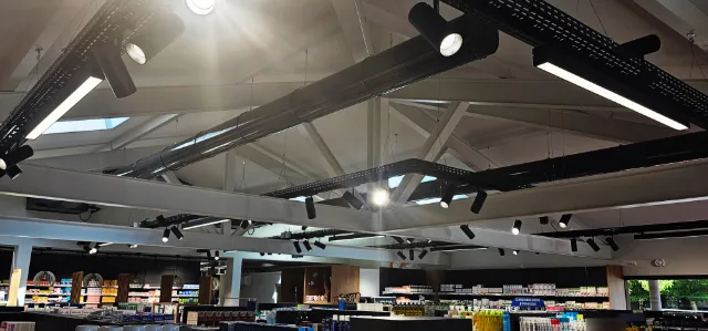Surface de vente sous charpente blanche, chemins de câbles noirs portant projecteurs et luminaires linéaires