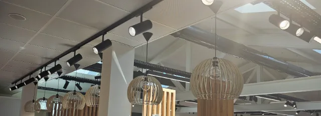 Plafond avec rail de spots noirs allumés et suspensions globes en lattes de bois