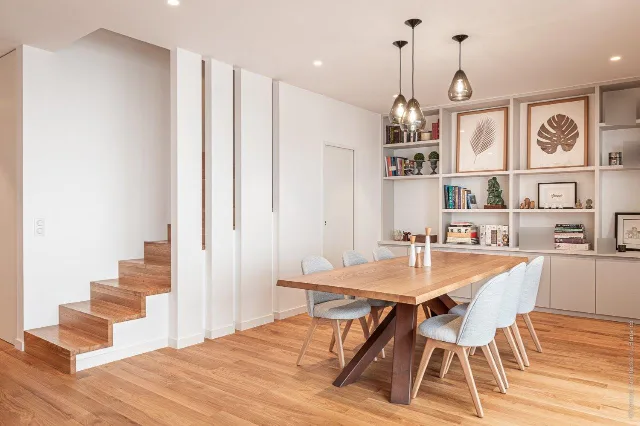 Salle à manger avec table en bois, trois suspensions en verre fumé et escalier en bois