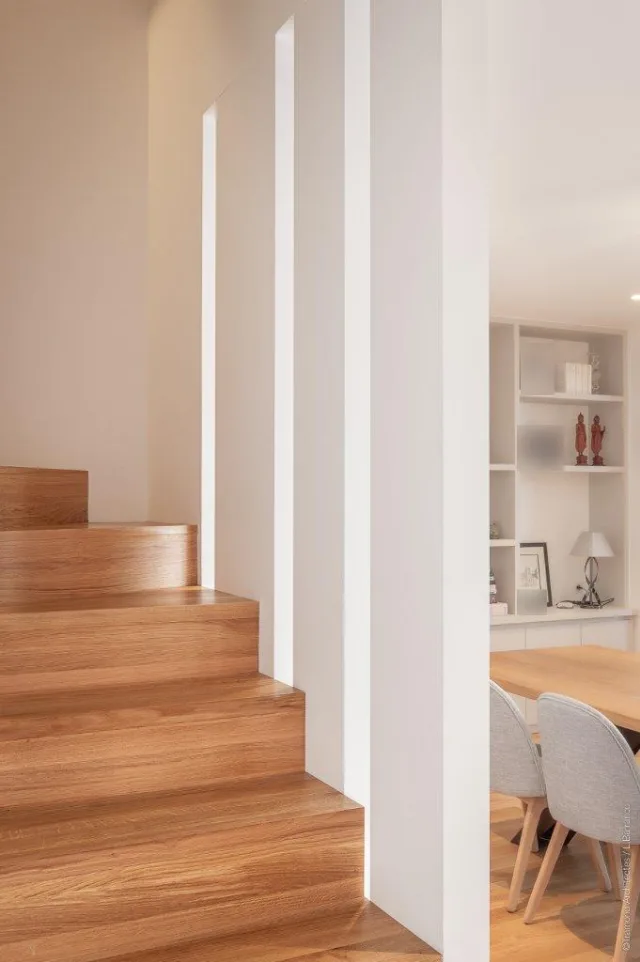 Escalier en bois bordé de lames verticales blanches, coin repas et étagères en arrière-plan