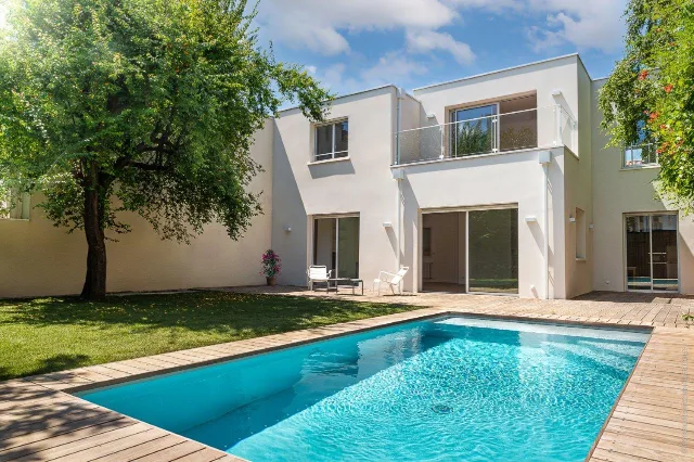 Maison blanche à toit plat, piscine bordée de bois, pelouse et grand arbre