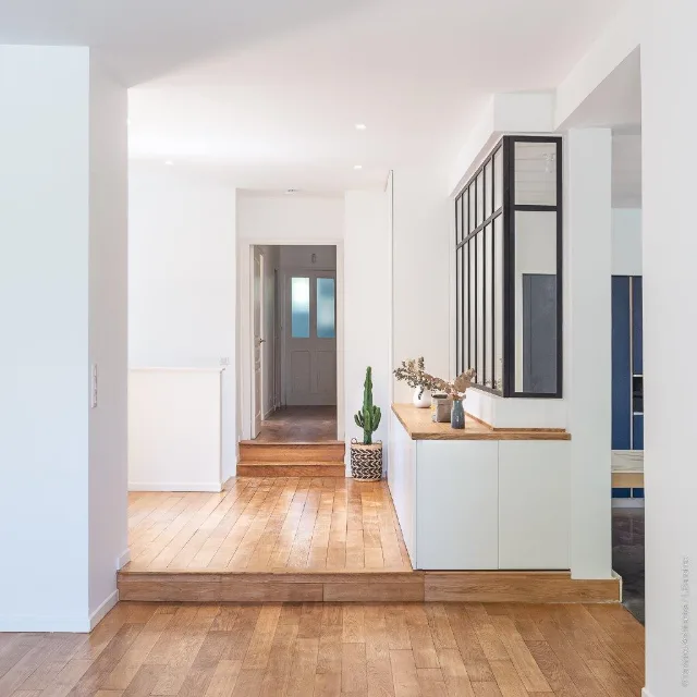 Couloir en parquet avec marches vers une porte vitrée, verrière noire et spots encastrés