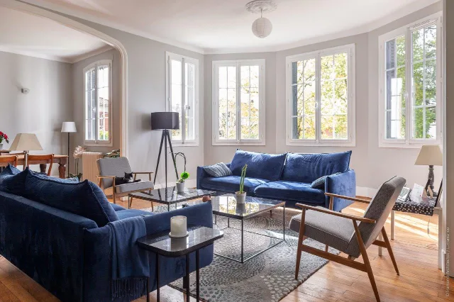 Salon en rotonde avec canapés en velours bleu, fauteuils, lampadaire trépied et suspension globe