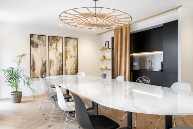 Pièce à grande table effet marbre, suspension en lamelles de bois, kitchenette noire éclairée par LED