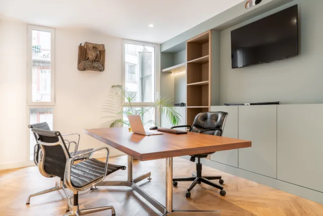 Bureau avec table en bois, fauteuils en cuir noir, meubles vert sauge et téléviseur mural